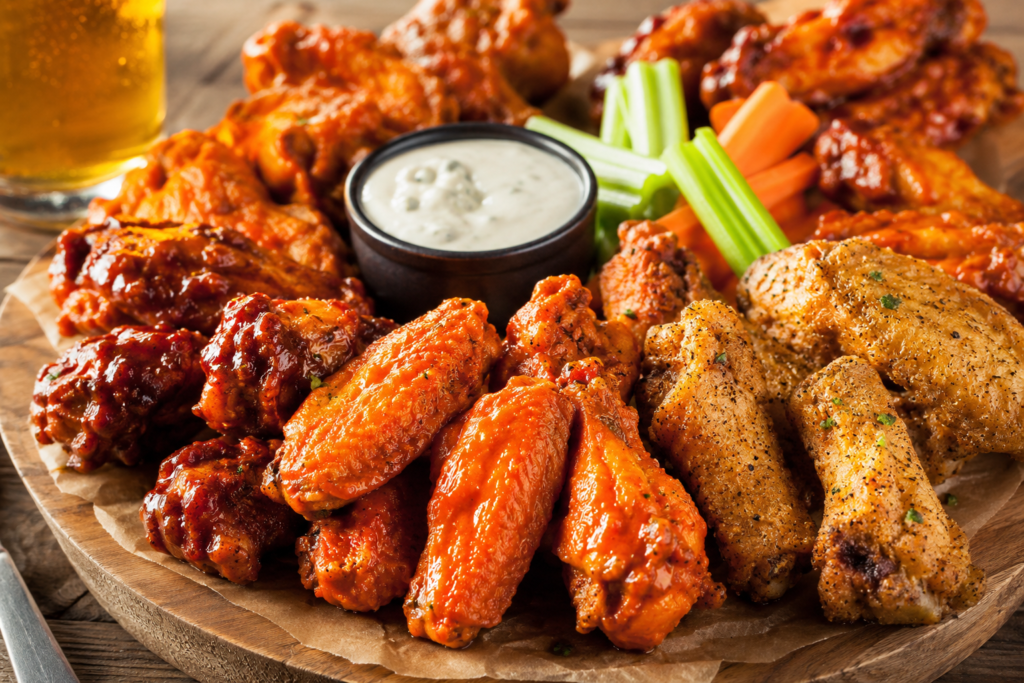 National Chicken Wing Day: The True History Behind July 29, Origins & How to Celebrate Assorted crispy chicken wings in Buffalo, barbecue, and dry-rub flavors served with creamy dipping sauce, celery sticks, and carrot sticks on a rustic wooden platter.