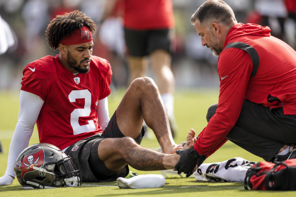 Buccaneers WR Emeka Egbuka Suffers Minor Toe Injury Ahead of 2026 Season Emeka Egbuka sits on the football field while a trainer examines his injured foot during Buccaneers practice.